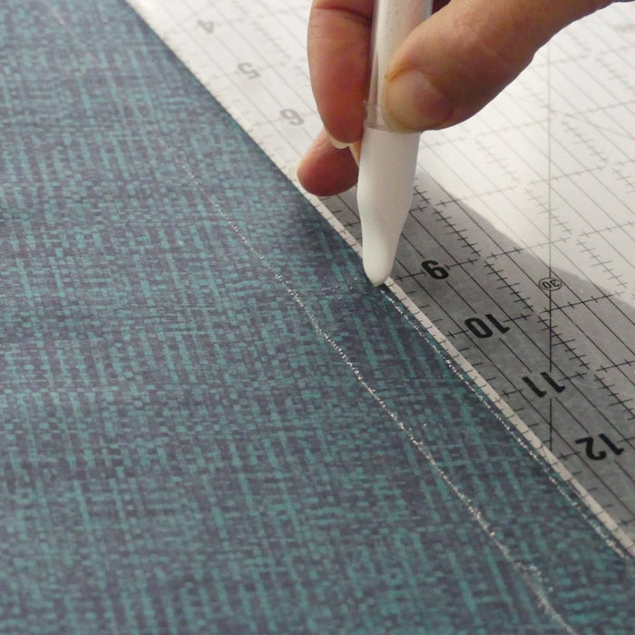Drawing a line with a white chalk marker  and a quilt ruler on dark fabric