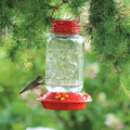Mason Jar Glass Hummingbird Feeder with clear glass reservoir and four flower feeding ports, shown with a hummingbird feeding.