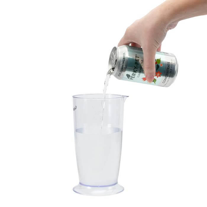 Hand pouring Perky-Pet® Clear Hummingbird Nectar Concentrate from a can into a glass, showcasing the product's easy-to-use feature.