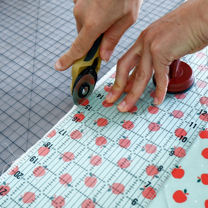 hands cut fabric with a rotary cutter and a ruler